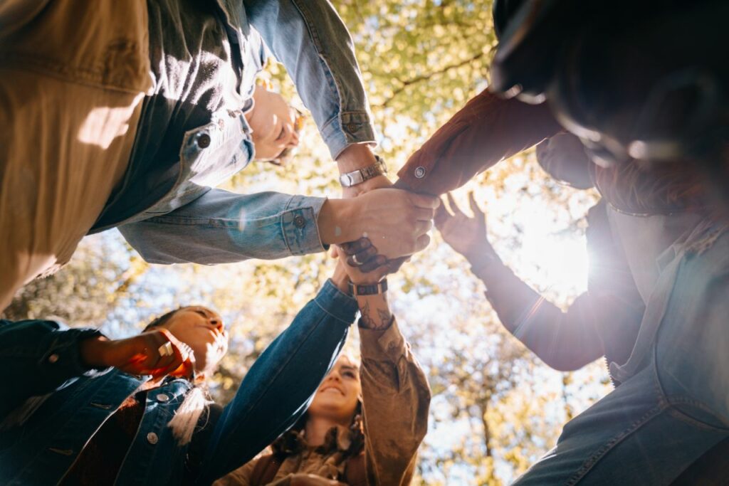 A diverse group of adults holding hands in unity and friendship under daylight.